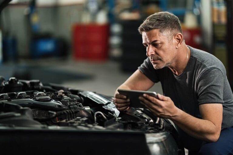mecânico com um tablet analisando o carro com o capô aberto